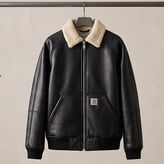 Blouson noir en cuir ou similicuir suspendu sur cintre, doté d'un col en mouton synthétique crème et du logo Carhartt.