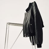 Blouson en cuir noir de coupe bomber ou perfecto, posé élégamment sur une chaise métallique épurée.