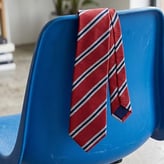 Cravate rouge à rayures obliques bleues et blanches, posée sur le dossier d'une chaise en plastique bleu.