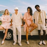 Quatre personnes posent devant une voiture blanche en bord de mer, vêtues de tenues estivales aux tons pastel et blancs.