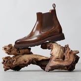 Bottine Chelsea en cuir marron glacé avec finitions perforées style brogue, présentée sur un morceau de bois flotté.