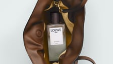 Vue en plongée d'un sac Loewe en cuir marron ouvert, révélant un flacon de parfum "Aire Sutileza" à l'intérieur. L'association des matières, cuir et bois, évoque un luxe naturel et épuré.