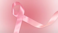 Un ruban en satin rose, symbole de la lutte contre le cancer du sein, est disposé en boucle au centre de l'image sur un fond dégradé d'un rose doux et lumineux.