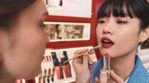 Une maquilleuse applique du rouge à lèvres au pinceau sur une jeune femme asiatique à frange.