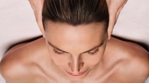 Cette image montre une femme allongée, vue du dessus, recevant un massage du cuir chevelu