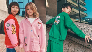 Trois enfants posent en vêtements colorés Kenzo devant un bâtiment moderne en béton et verre.