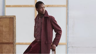 Homme portant un manteau en laine bordeaux structuré sur une chemise à motifs et un pantalon en velours côtelé.