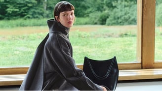 Femme portant un manteau long en laine gris à col montant structuré devant une baie vitrée