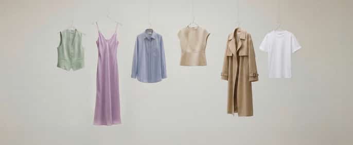 L'image montre six vêtements minimalistes suspendus sur un fond neutre : un gilet, une robe lilas, une chemise, un haut, un trench-coat beige et un t-shirt blanc.