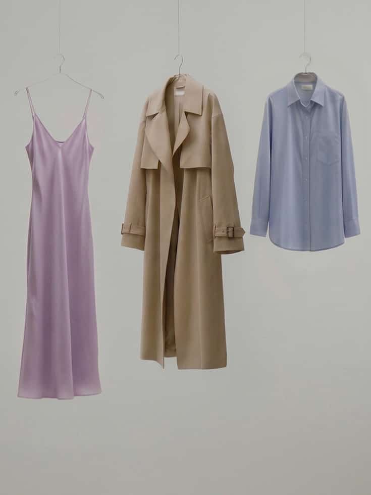 L'image montre six vêtements minimalistes suspendus sur un fond neutre : un gilet, une robe lilas, une chemise, un haut, un trench-coat beige et un t-shirt blanc.